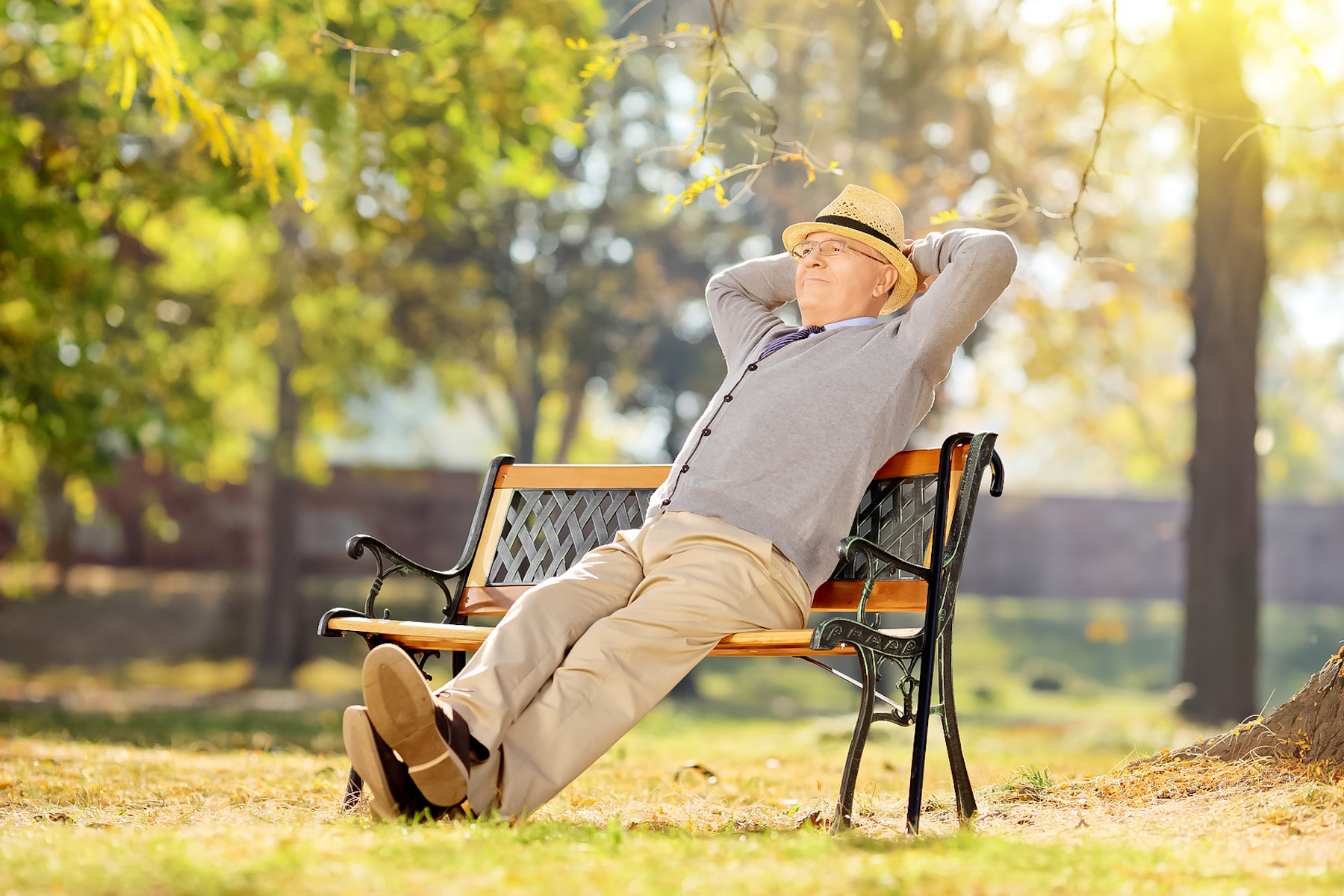 Senior man relaxing in park on a sunny day seated on a wooden bench